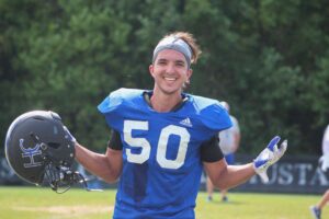 Theo Constantinou grinning and wearing a blue football jersey with the number 50 on it.